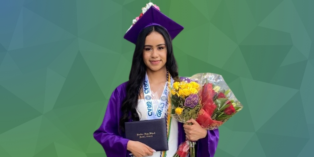 smiling student in cap and gown holding diploma and flowers