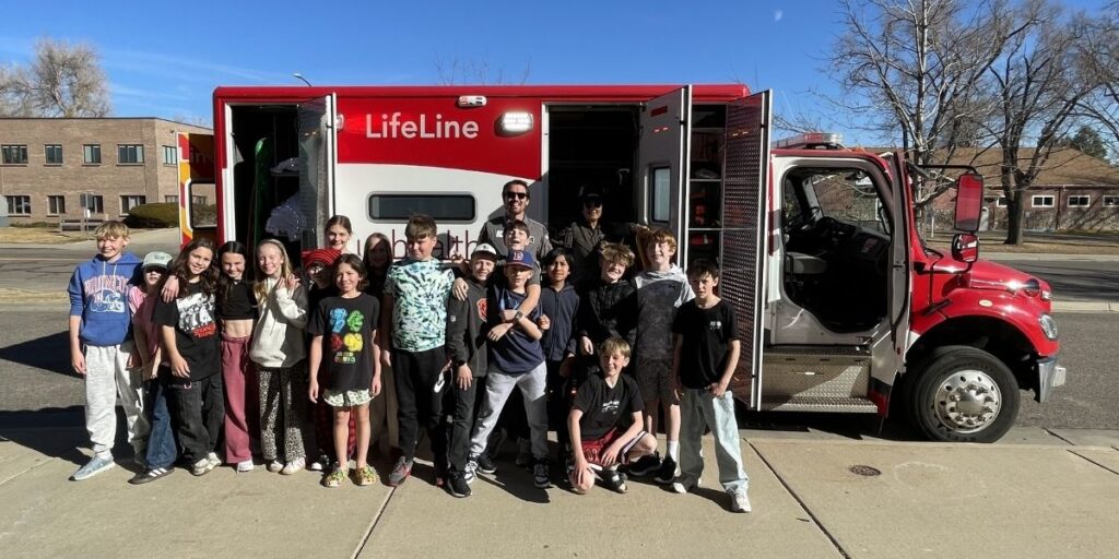 group of smiling middle school students and emergency medical professional with ambulance